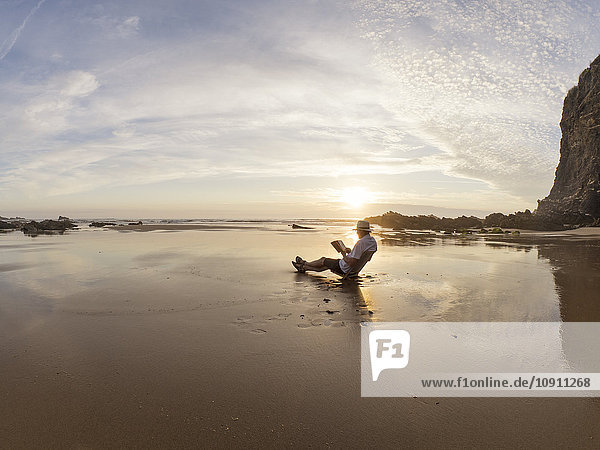 Portugal  Senior am Strand sitzend  Lesebuch