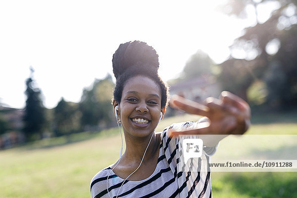Portrait of happy woman hearing music with earphones showing victory sign
