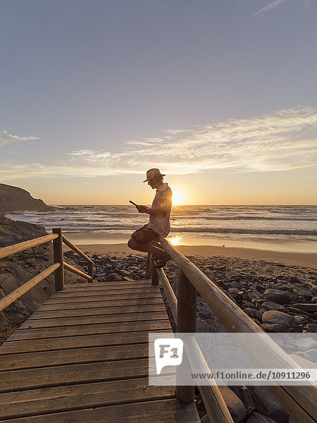 Portugal  älterer Mann auf einem Geländer am Strand sitzend  lesend