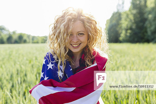 Porträt einer lächelnden Frau mit amerikanischer Flagge in der Natur