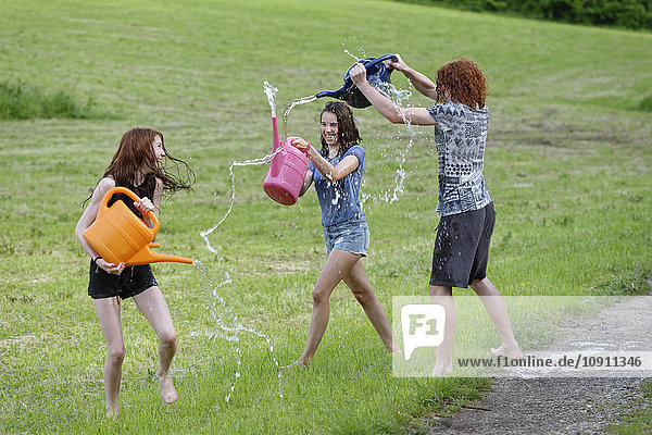 Drei Teenager mit Gießkannen  die mit Wasser spritzen.