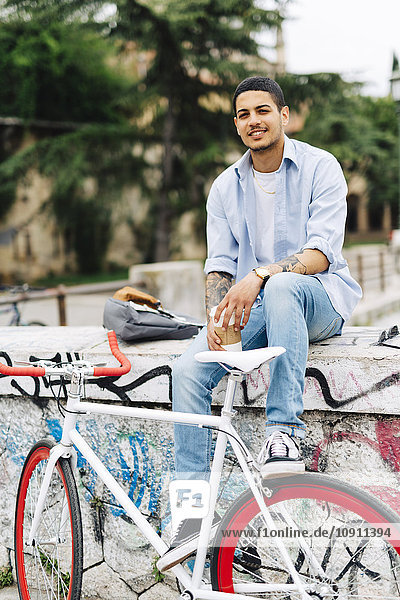 Smiling young man with a bicycle sitting on graffiti wall