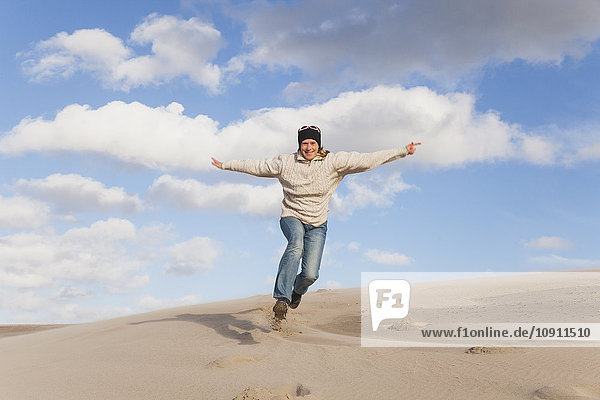 Begeisterte reife Frau beim Laufen und Springen auf der Sanddüne