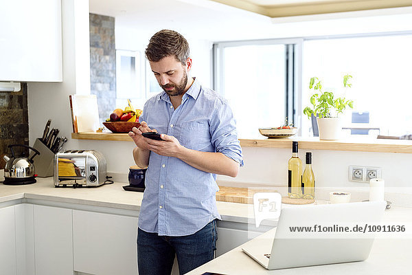 Man working in kitchen using smart phone