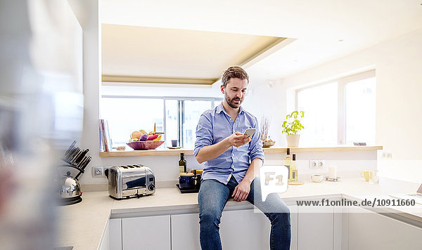 Man sitting in kitchen using smart phone