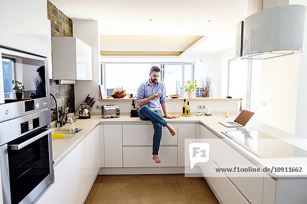 Mann sitzt in der Küche mit Smartphone