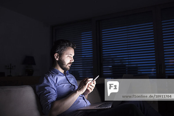 Man working at night using smart phone and laptop