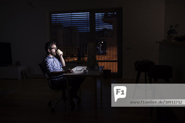 Man working at computer and drinking coffee at night