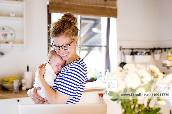 Happy mother with baby in kitchen looking at laptop