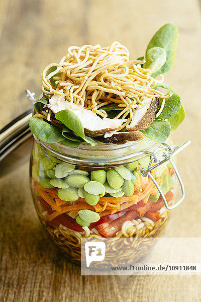 Asiatischer Salat im Glas mit Ramen-Nudeln  rotem Pfeffer  Erbsenschoten  Karotten  Edamame  Shiitake-Pilzen  Salatgrün  gebratenen Chow-Mien-Nudeln und Dressing