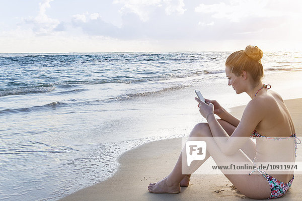 Dominican Rebublic  Junge Frau am tropischen Strand mit mobilem Gerät