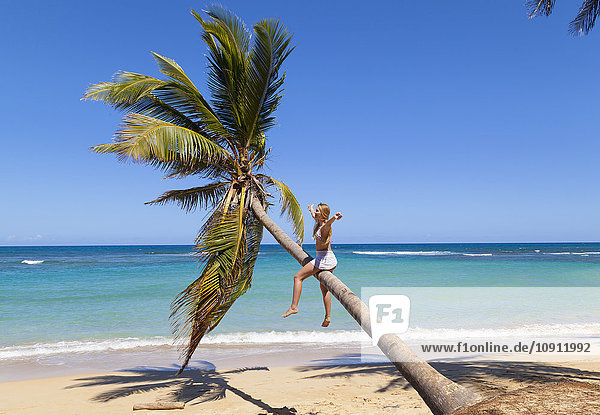 Dominikanische Rebublik  Junge Frau klettert auf Palme am tropischen Strand