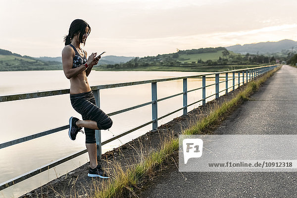 Sportlerin beim Überprüfen von Smartphones am Geländer