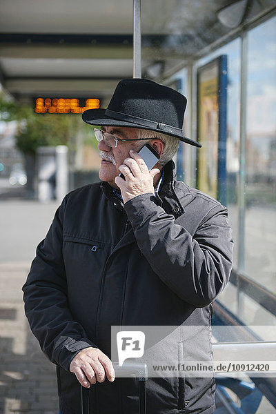 UK  Bristol  Senior Mann telefoniert mit Smartphone während er an der Bushaltestelle wartet.