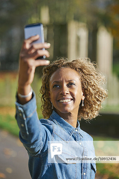 Porträt einer lächelnden Frau  die sich selbst mit dem Smartphone fotografiert.