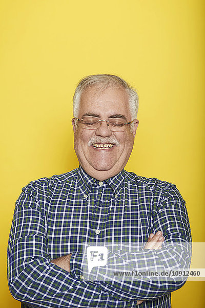 Porträt eines lächelnden älteren Mannes mit gekreuzten Armen und geschlossenen Augen vor gelbem Hintergrund
