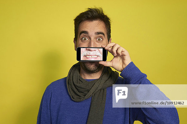 Porträt eines Mannes  der ein Smartphone hält  mit der Fotografie des lächelnden Mundes eines anderen Mannes.