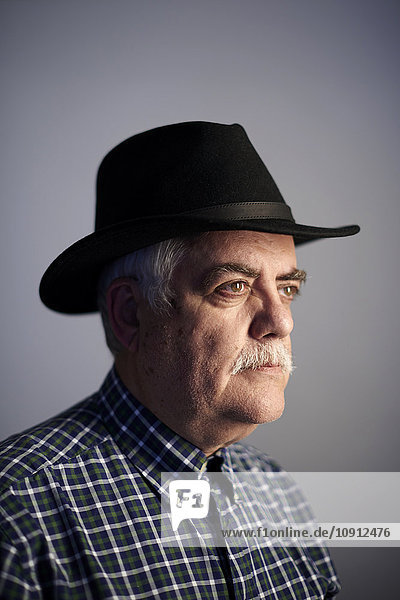 Porträt eines ernsthaften älteren Mannes mit schwarzem Hut vor grauem Hintergrund