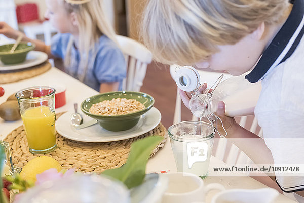 Boy pouring milk into glass at breakfast table