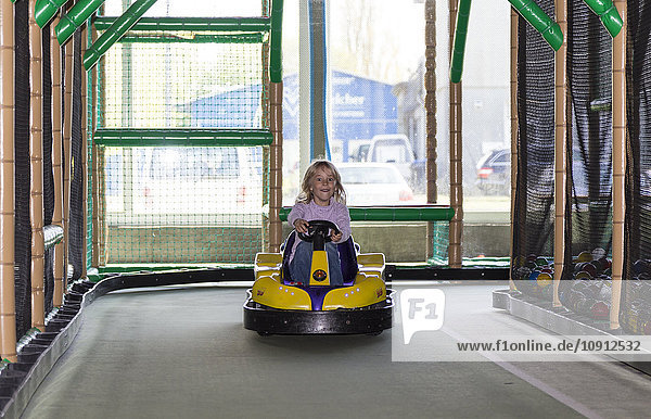 Aufgeregtes kleines Mädchen beim Autofahren auf einem Indoor-Spielplatz