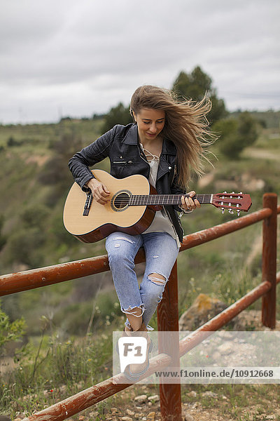 Frau auf Holzzaun sitzend Gitarre spielend