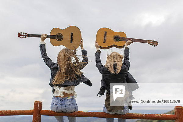 Zwei Frauen sitzen auf einem Holzzaun und heben Gitarren hoch.