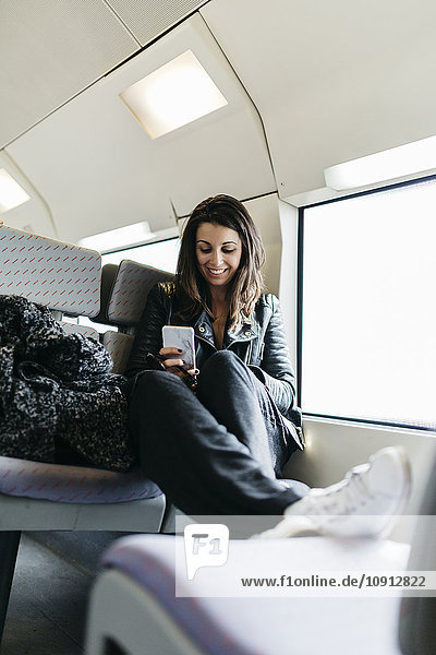 Lächelnde junge Frau im Zug mit Blick aufs Handy