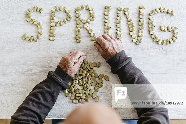 Man putting the word 'spring' with dried beans on tabletop