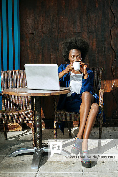 Young woman with laptop sitting in a street cafe drinking coffee