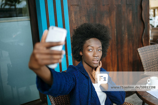 Portrait of young woman taking a selfie with smartphone in a street cafe