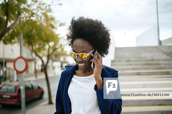 Porträt einer jungen Frau mit verspiegelter Sonnenbrille im Gespräch auf dem Handy