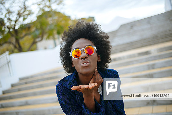 Portrait of young woman wearing mirrored sunglasses throwing a kiss to camera