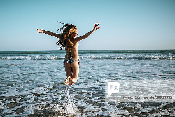 Begeisterte junge Frau beim Springen am Strand