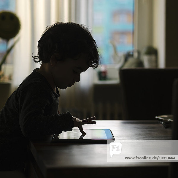 Silhouette eines kleinen Mädchens,  das zu Hause mit einem digitalen Tablett spielt.
