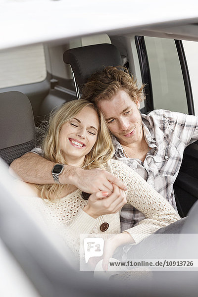 Verliebtes junges Paar sitzt im Auto und hält sich an den Händen.