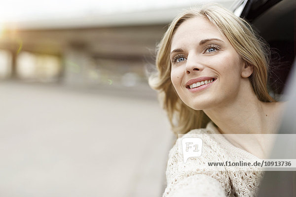 Porträt einer lächelnden jungen Frau  die sich aus dem Autofenster lehnt und etwas beobachtet.