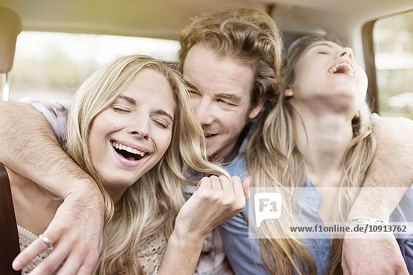 Drei lachende Freunde  die auf dem Rücksitz des Autos sitzen und Spaß haben.