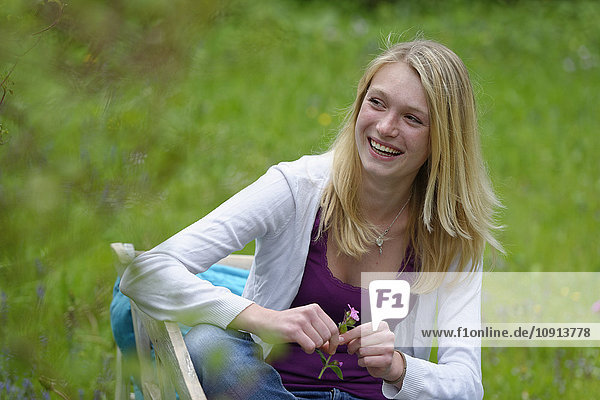 Porträt einer lachenden blonden Frau auf einer Bank in der Natur