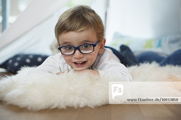 Little boy with glasses lying on sheepskin
