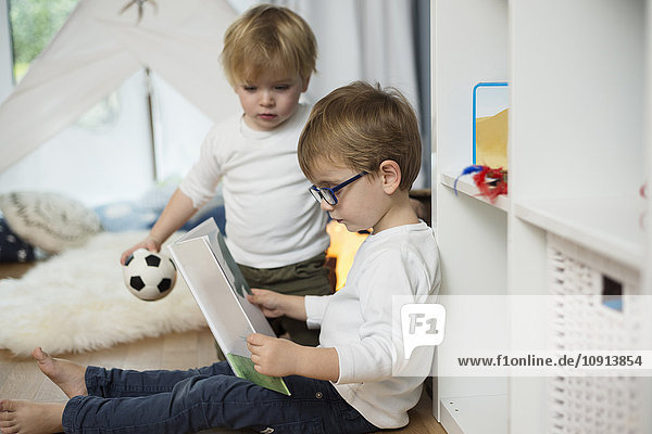 Two little boys playing at home  looking at picture book