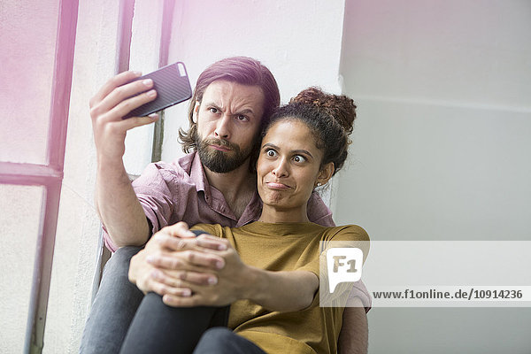 Junges Paar sitzt auf der Fensterbank und nimmt Selfie mit Smartphone