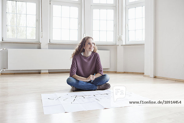Smiling woman with construction plan in empty apartment