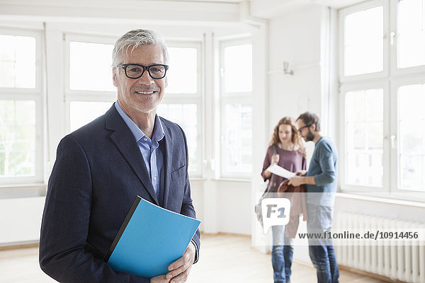 Portrait of smiling real estate agent with couple in background