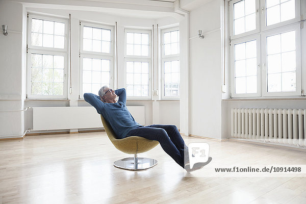 Entspannter Mann sitzt im Sessel in leerer Wohnung