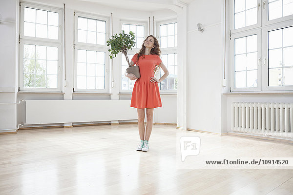 Smiling woman holding plant in empty apartment
