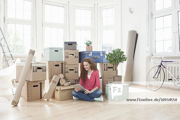 Woman surrounded by cardboard boxes using digital tablet