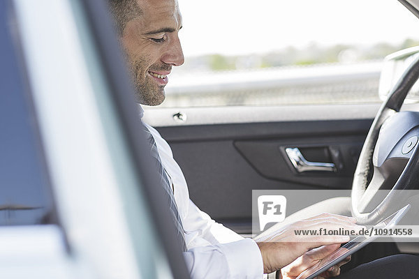 Lächelnder Geschäftsmann mit digitalem Tablett im Auto
