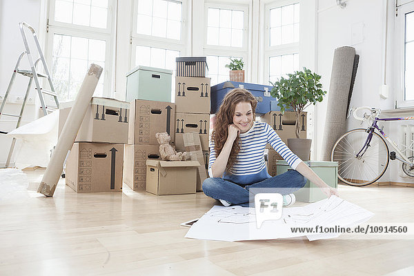 Woman surrounded by cardboard boxes sitting on floor looking at construction plan