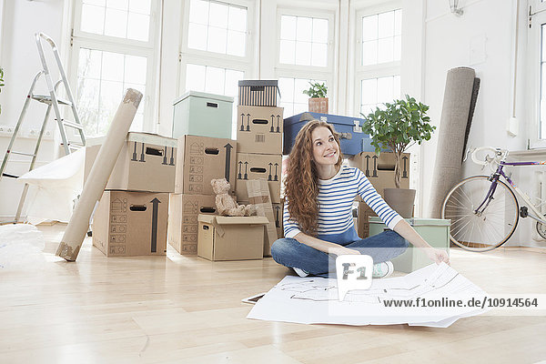 Woman surrounded by cardboard boxes sitting on floor with construction plan