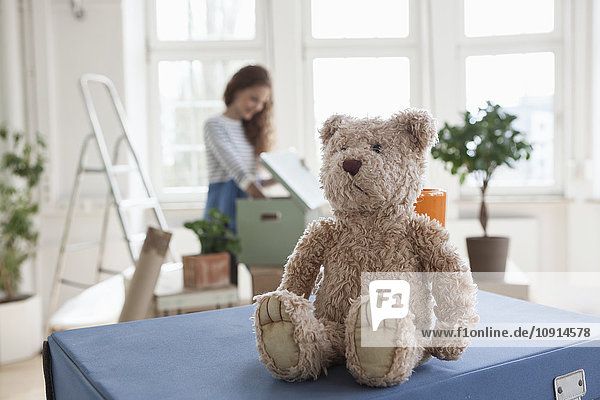 Teddy on cardboard box with woman in background